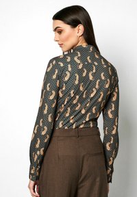 Long-sleeve shirt with a dark green background, featuring a gold paisley pattern and small blue dots. Smooth fabric, tailored fit.