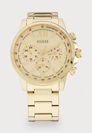 Montre-bracelet Guess ton or avec lunette tachymètre, trois sous-cadrans affichant l'heure sur 24 heures, le jour de la semaine et la date, sur un bracelet en métal à maillons.