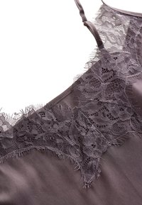 Camisole di raso grigio scuro con bordo in pizzo intricatamente lavorato. Presenta spalline regolabili e delicati bordi sfrangiati lungo il pizzo. Texture liscia.