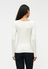 Λευκή μπλούζα με μακριά μανίκια, ριγωτή �υφή, μποτνέκ και εφαρμοστή γραμμή. Φορεμένη με σκούρο μπλε τζιν.