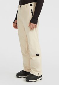 Beige sneeuwbroek van duurzame stof, met ritszakken, een rechte pijp ontwerp en een logo patch nabij de zoom.