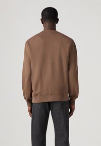 Bruine crewneck sweatshirt van zacht materiaal, met geribde manchetten en zoom, in een relaxte pasvorm, gedragen met donkere jeans.