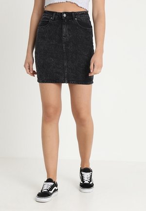Jupe en denim noir avec un design ajusté, cinq poches, fermeture à boutons sur le devant, et une texture légèrement délavée, associée à des baskets noires.