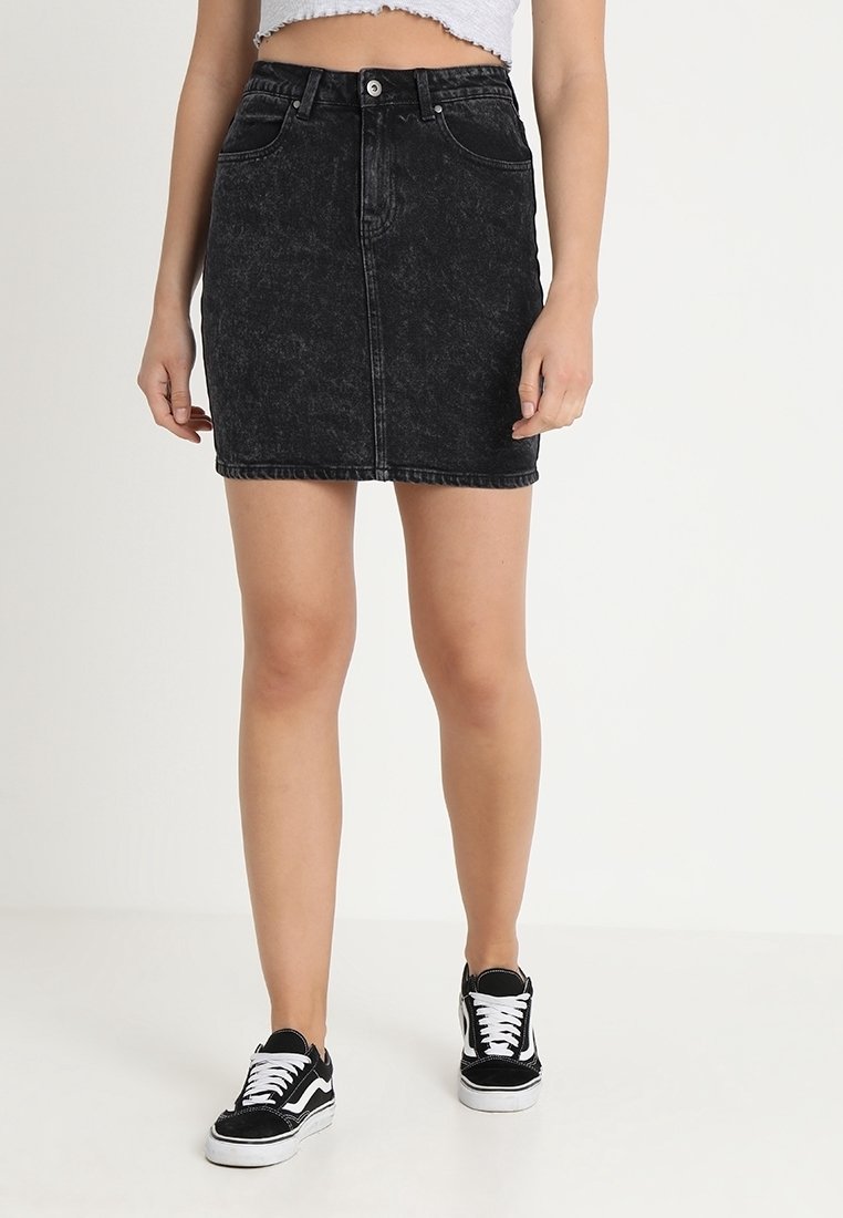 Falda de mezclilla negra con un diseño ajustado, cinco bolsillos, cierre de botón frontal y una textura ligeramente deslavada, combinada con zapatillas negras.
