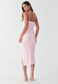 Pink midi-kjole med spaghetti-stropper, tætsiddende design og sideslids, lavet af et glat stof. Har en dyb ryg.