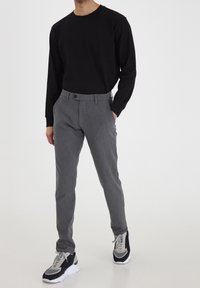 Pantalones gris texturizados con un corte recto, bolsillos delanteros y cierre de botón, combinados con una camisa negra de manga larga y zapatillas multicolores.