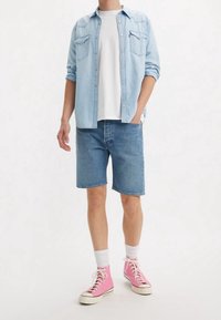 Camisa de mezclilla azul claro con botones a presión, camiseta blanca, pantalones cortos de mezclilla azul y zapatillas altas rosas con suelas de goma blanca y cordones.