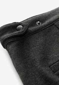Gros plan d’un tissu gris foncé avec une fermeture à bouton-pression noir sur une manchette ou le bord d’un rabat.