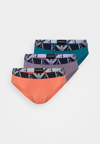 Kolme paria naisten alushousuja: oranssi, teal ja violetti. Ominaisuuksiin kuuluu mustavalkoinen logoelastinen vyötärö, jossa on geometrinen kuvio.