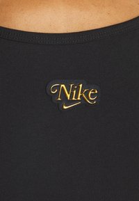 Zwarte stof met een ribbelstructuur, voorzien van een gouden Nike-logo patch aan de voorkant. Glad, aansluitend ontwerp.