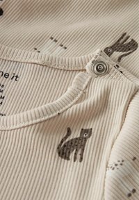 Beżowa prążkowana tkanina z małymi nadrukami kotów. Posiada zatrzask przy dekolcie. Miękka faktura i prosty design.