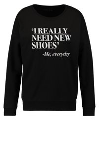 Sudadera negra de manga larga con texto blanco que dice "'REALMENTE NECESITO ZAPATOS NUEVOS' -Yo, cada día" en el centro del frente.