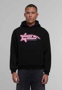 Sudadera negra de algodón, con un logotipo gráfico rosa en forma de estrella. El diseño incluye un bolsillo frontal y puños acanalados.