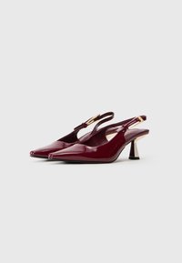 Burgundijas lakota āda slingback augstpapēžu kurpes ar smailiem purngaliem un zelta tonētiem sprādžu akcentiem uz balta fona.