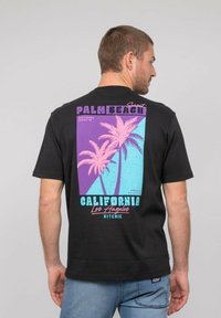 T-shirt noir à manches courtes avec un design graphique rétro featuring des palmiers, des couleurs pastel (rose, violet, aqua) et des éléments de texte au dos.