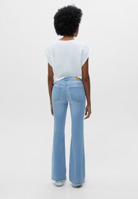 Jean évasé bleu clair avec une taille mi-haute et deux poches arrière, associé à un haut gris clair à manches courtes. Texture lisse.