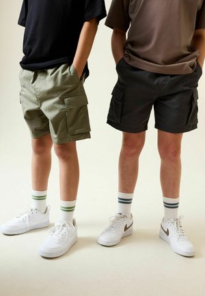 Twee paar shorts: olijfgroen en zwart, beide met cargozakken. Draag ze met witte sneakers en gestreepte enkelsokken. Casual pasvorm.