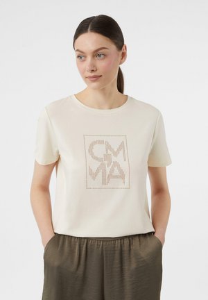 Beige T-Shirt mit kurzen Ärmeln, ausgestattet mit einem quadratischen Design und gepunkteter Schrift in Braun. Weicher Stoff, lockere Passform, kombiniert mit olivgrünen Hosen.