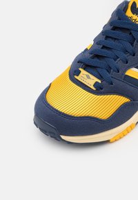 Niebiesko-żółty but sportowy Adidas z granatowymi sznurówkami i metką "TORSION" na żółtym prążkowanym nosku, pokazany pod kątem z przodu z boku.