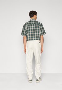 Chemise à manches courtes à carreaux verts et blancs, assortie à un pantalon beige. Caractérisée par une coupe décontractée et une silhouette droite.
