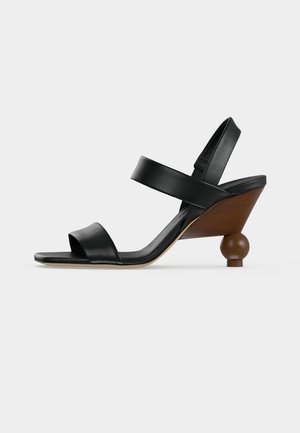Sandale noire en cuir à bout ouvert avec deux brides et un talon compensé en bois avec une base ronde en forme de boule.