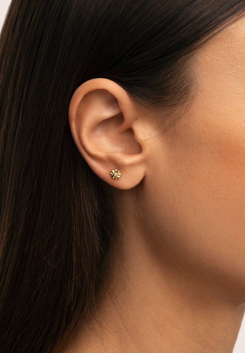 Boucles d'oreilles en or avec un design floral, présentant de petites pierres au centre. Texture lisse, forme compacte et style minimaliste.