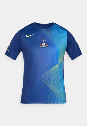 Blauwe sportshirt van gladde stof met een clublogo op de borst en een dynamisch groen golvenpatroon over de voorkant.