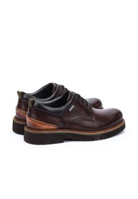 Chaussures en cuir marron avec une finition lisse, bout rond, accents beiges contrastants, lacets noirs et semelle en caoutchouc texturée. Design minimaliste.