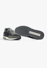 Sneaker sportive con un design grigio scuro e verde oliva, caratterizzate da una tomaia in suede e rete, chiusura con lacci e suola in gomma testurizzata.