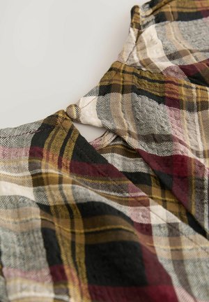Lähellä oleva kangas, jossa on ruutukuosi maanläheisissä punaisen, keltaisen, mustan ja harmaan sävyissä, sisältäen kaula-aukon yksityiskohtia.