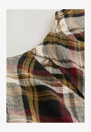 Lähellä oleva kangas, jossa on ruutukuosi maanläheisissä punaisen, keltaisen, mustan ja harmaan sävyissä, sisältäen kaula-aukon yksityiskohtia.