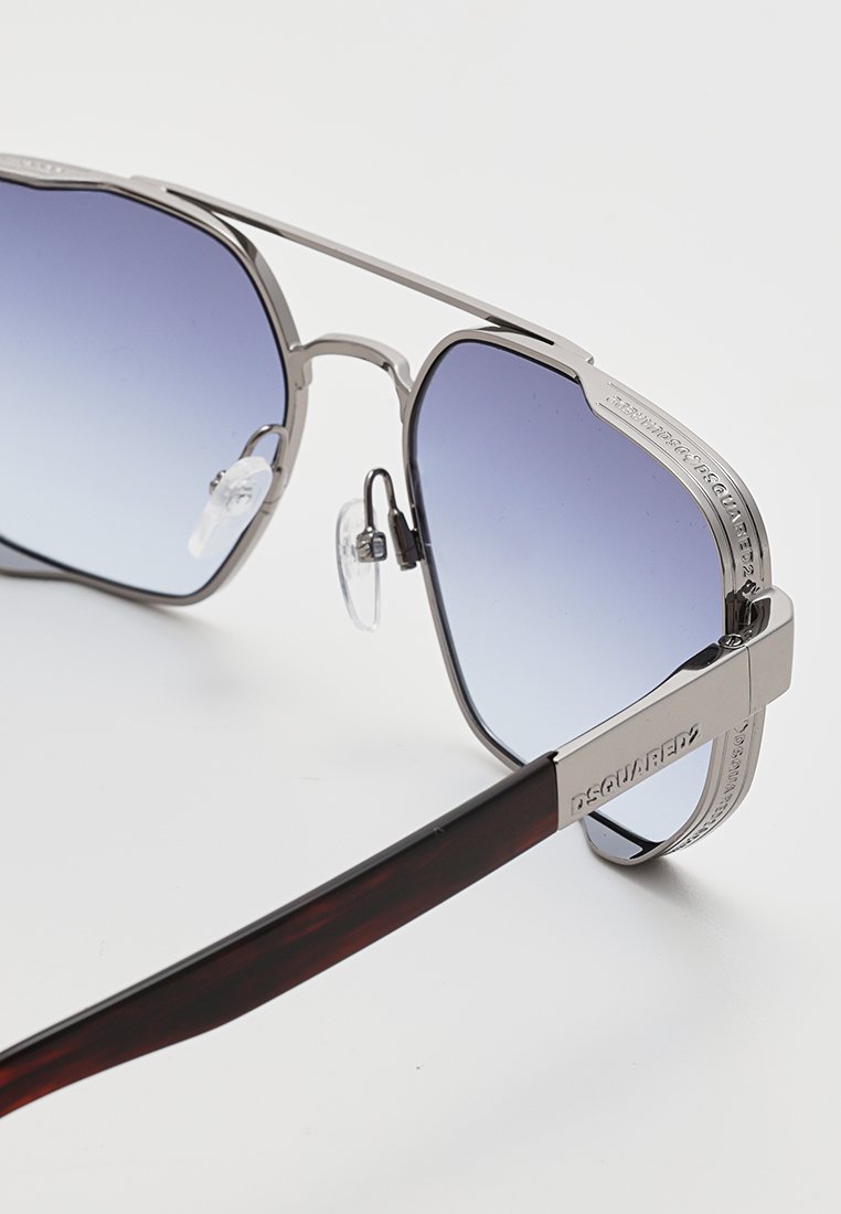 Silverfärgade metallsolglasögon med gradientblå linser. Fyrkantig båge med klara näskuddar. Skalmens insida har en mörk sköldpaddsfinish och varumärkeslogotyp.