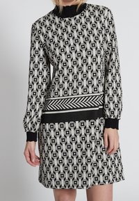 Abito in bianco e nero con motivi geometrici, maniche lunghe, collo alto e una cintura a righe contrastanti.