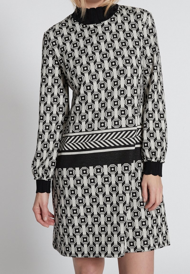 Abito in bianco e nero con motivi geometrici, maniche lunghe, collo alto e una cintura a righe contrastanti.