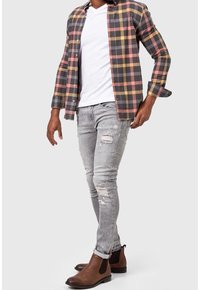 Button-up Karohemd in Grau, Pink und Gelb, kombiniert mit abgeranzten grauen Jeans und braunen Chelsea-Boots. Geschmeidige Stoffstruktur und taillierte Passform.