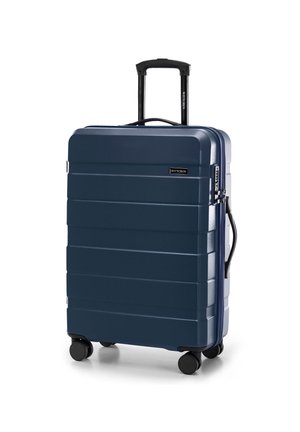 Valise rigide navy avec des rainures verticales, poignée télescopique et quatre roues noires. Présente un emblème de logo à l'avant.