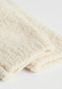 Materiał w kolorze kremowym z teksturą i puszystą powierzchnią, starannie złożony. Splot ma subtelny wzór, co zwiększa jego jakości dotykowe.