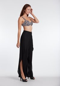 Black high-waisted trousers with side slits paired with a patterned black and white bikini top featuring wide straps and a structured design.
