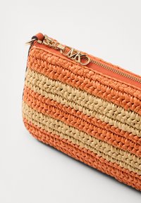 Pochette tissée avec des rayures orange et beige, dotée d'une fermeture éclair et de ferrures en or. Surface texturée avec une forme rectangulaire.