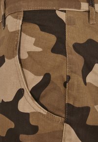 Close-up of brown, tan, and black camouflage fabric with detailed stitching and a curved front pocket seam.