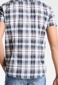 Camisa de manga corta con estampado de cuadros en tela ligera. Presenta cuadros en azul marino, blanco y rosa, con un ajuste relajado y un dobladillo curvado en la parte trasera.