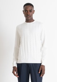 Maglione bianco con motivo testurizzato sul davanti, scollatura rotonda, maniche lunghe e orlo a costine. Abbinato a pantaloni blu navy.