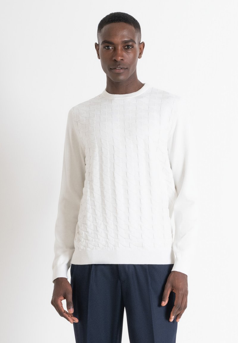 Maglione bianco con motivo testurizzato sul davanti, scollatura rotonda, maniche lunghe e orlo a costine. Abbinato a pantaloni blu navy.