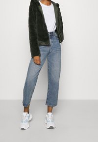 Puchata, ciemnozielona bluza z kapturem na zamek, biała koszulka pod spodem, jasnoniebieskie, krótkie dżinsy oraz białe trampki z szarymi akcentami.