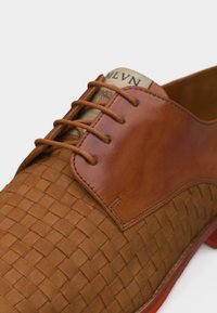 Chaussure habillée en cuir marron avec texture tissée sur l'avant et les côtés, cuir lisse près des lacets, et lacets marron assortis noués en un nœud.