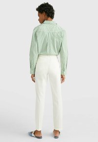 Maglietta a righe verde e bianca, taglio sartoriale, con spallina sul retro. Abbinata a pantaloni bianchi e sandali scivolati con dettagli blu.