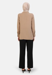 Beige blouse met lange mouwen en kraag, met knoopdetails op de mouwen, gecombineerd met zwarte wijde broek en zwarte hoge hakken.