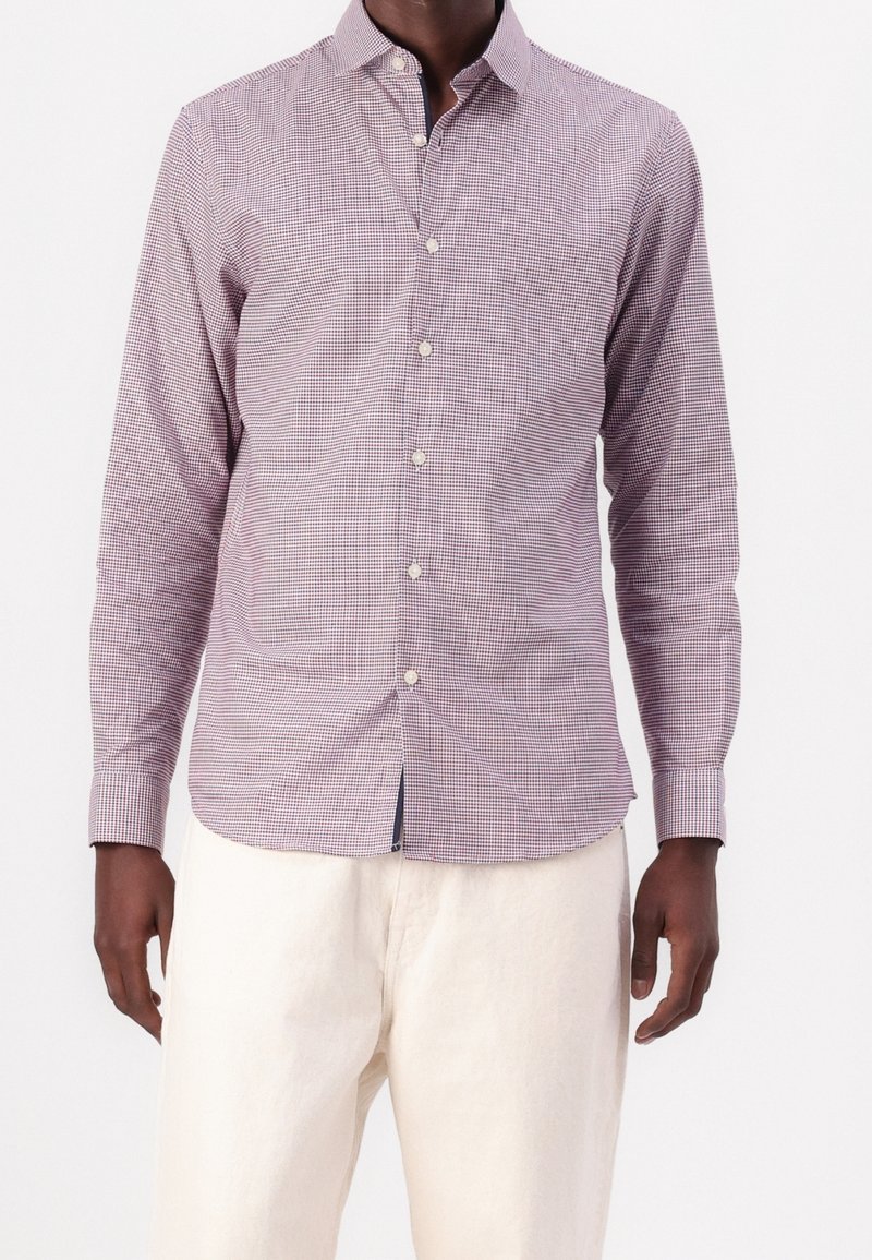 Camisa de cuadros de manga larga en tela morada y blanca, con diseño de botones, cuello puntiagudo y dobladillo curvo. Llevada con pantalones de color claro.