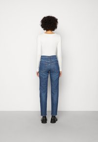 Bílá pruhovaná košile s dlouhým rukávem spárovaná s modrými denimovými džíny s vysokým pasem, které mají rovný střih a dvě zadní kapsy. Černé kotníkové boty.