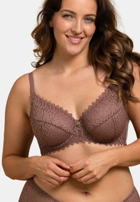 Soutien-gorge en dentelle mauve avec un motif géométrique, des bords festonnés et un bouton décoratif au centre, doté de bretelles réglables.